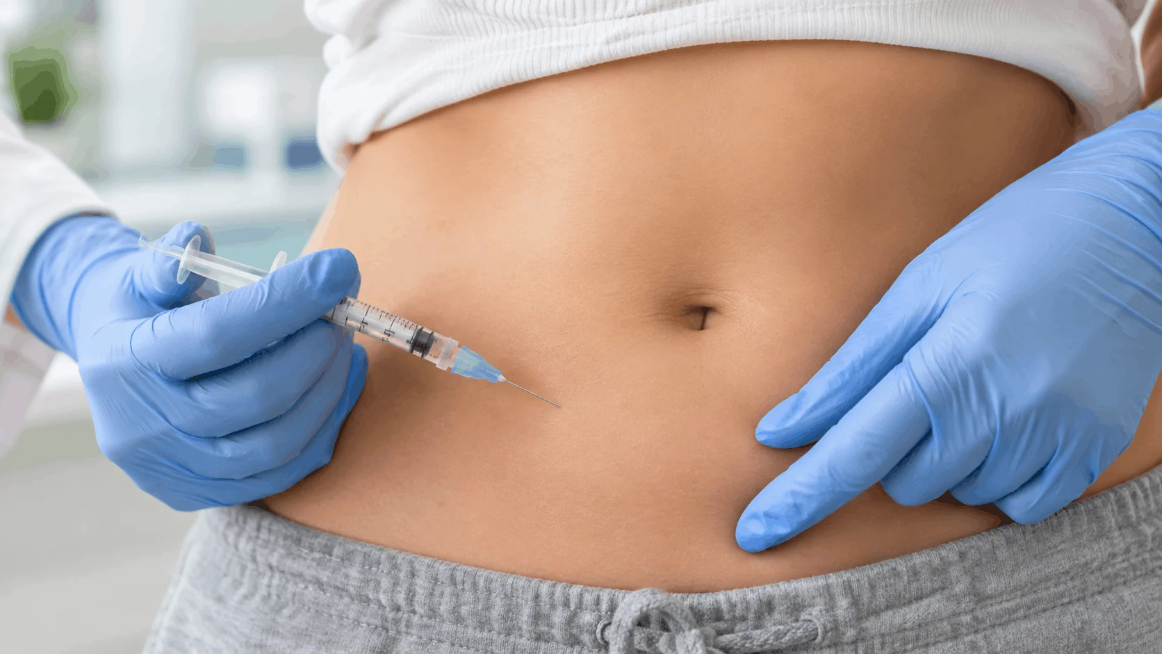 A healthcare provider holding a patient's abdomen while preparing to administer a weight loss injection.